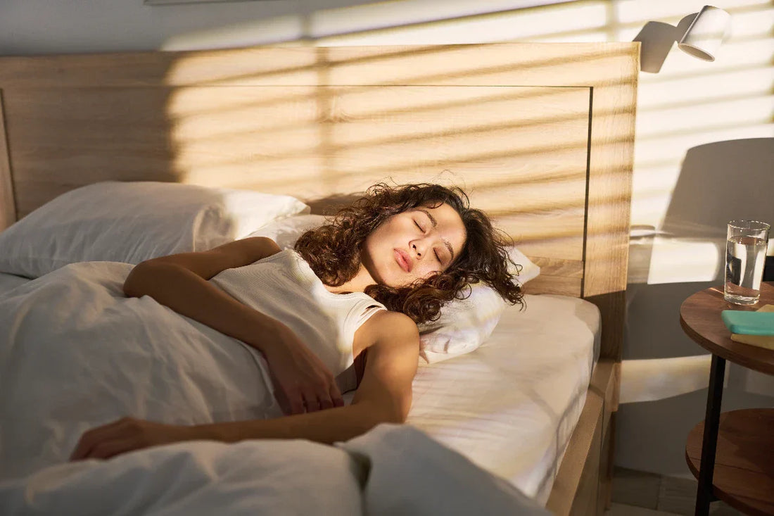 A woman sleeping in bed with the sun coming through the window.